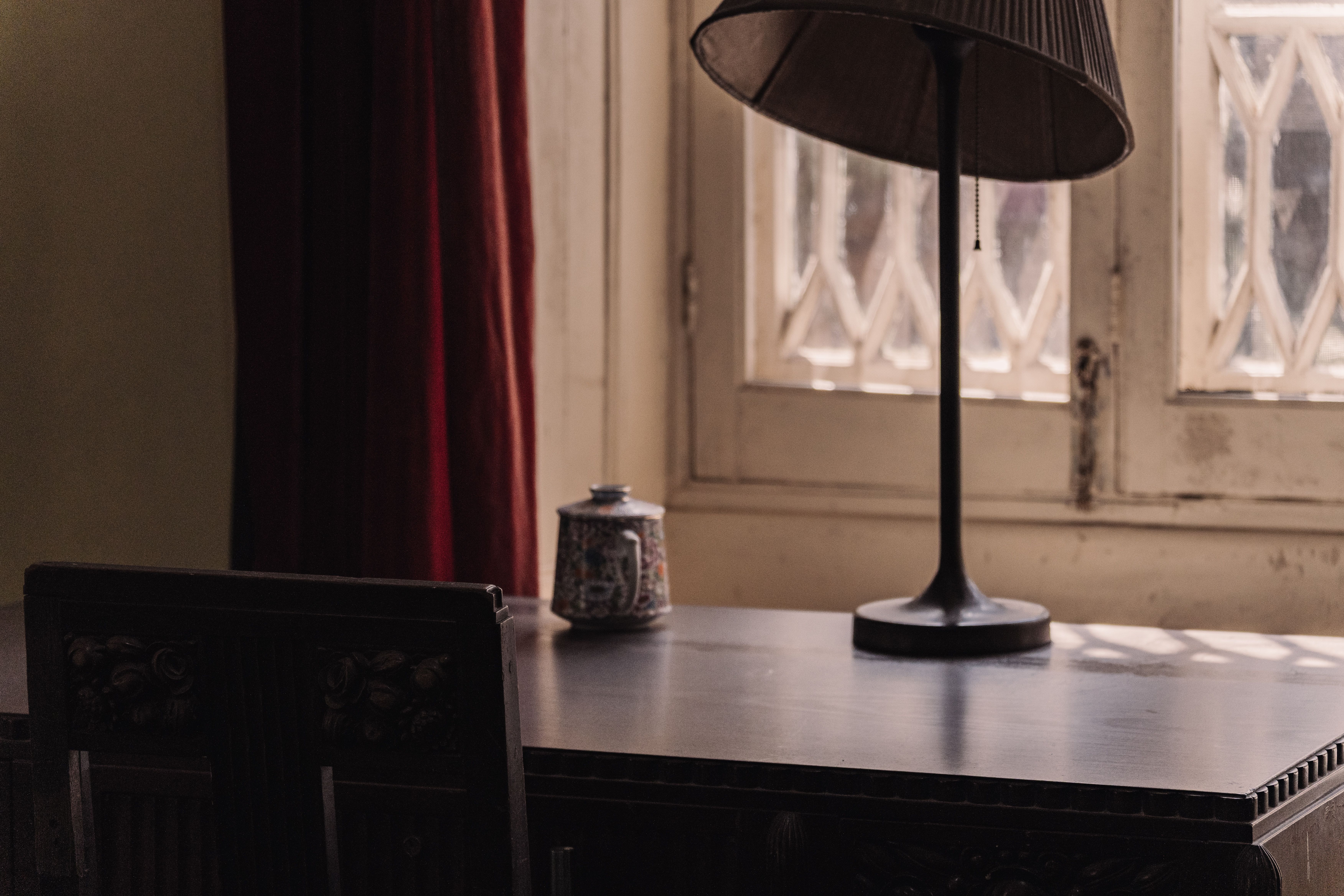 Lamplit writing desk beside a shuttered window in low evening light